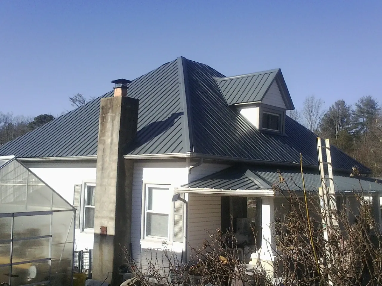 Dark blue standing seam metal roof on a white farmhouse with dormer — Slate & Tile Roof Repair by Roofing Brothers in Fort Morgan