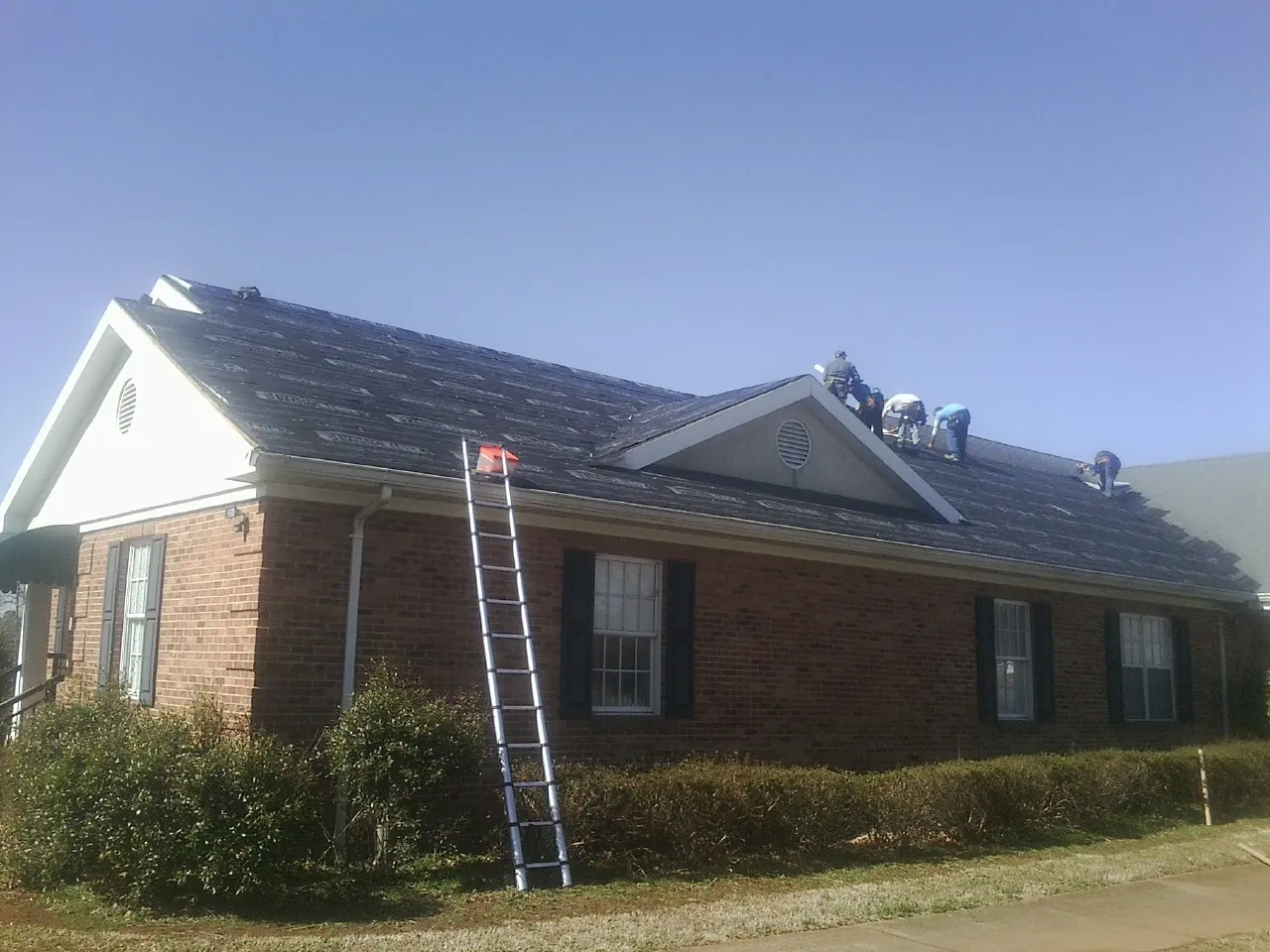Crew tearing shingles off a brick ranch roof with a ladder set — Metal Roof Repair work by our crew in Fort Morgan