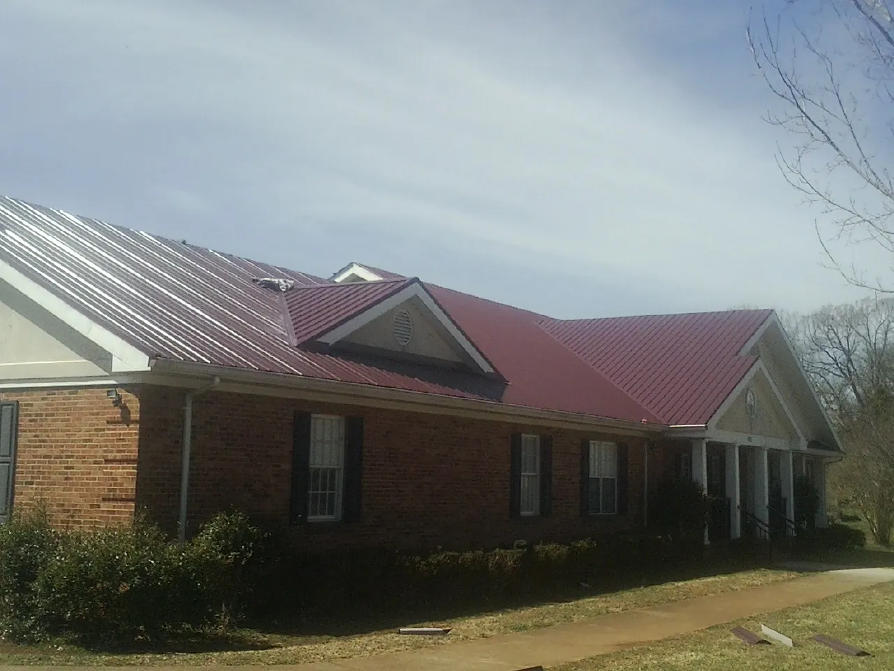 Red metal roof with gabled entries on a long brick building, from a Hail Damage Roof Repair job in Fort Morgan