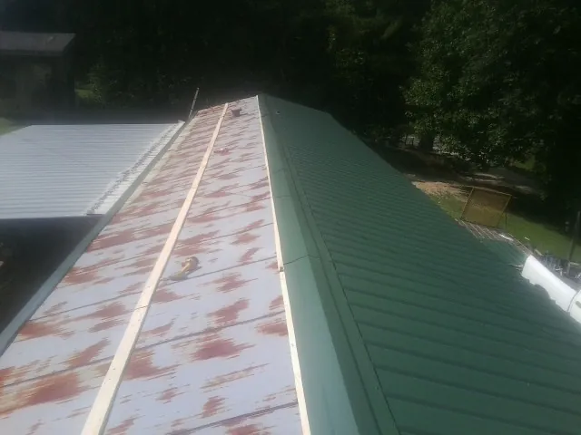 Old rusted panels beside newly installed green metal roofing — Wind Damage Roof Repair by Roofing Brothers in Fort Morgan