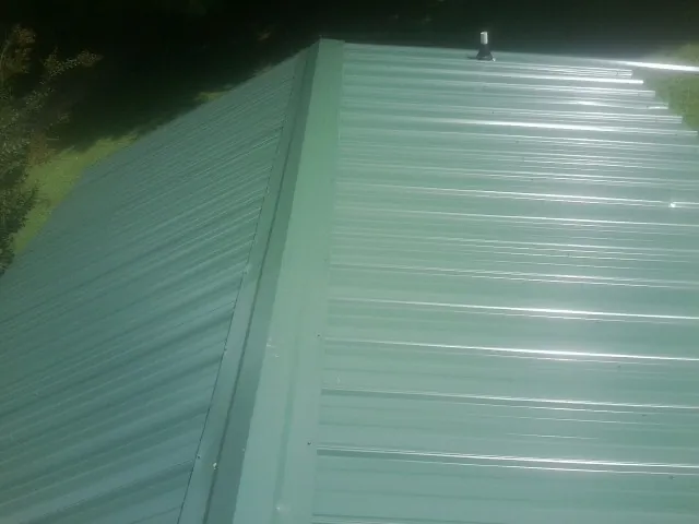 New green metal panels meeting at the ridge of a roof — Flat Roof Repair work by our crew in Fort Morgan