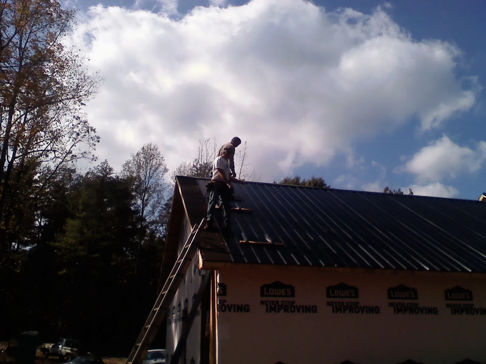 Roofer fastening dark metal panels high against a cloudy sky, from a Roof Inspection job in Fort Morgan
