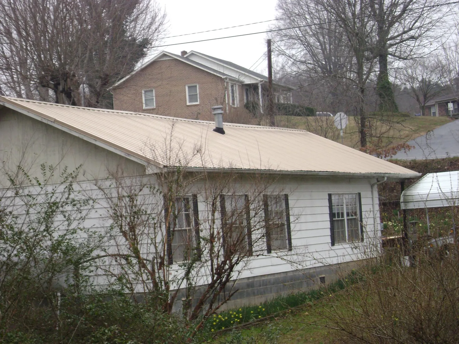 Tan metal roof on a white sided house set into a hillside — Commercial Roofing by Roofing Brothers in Fort Morgan