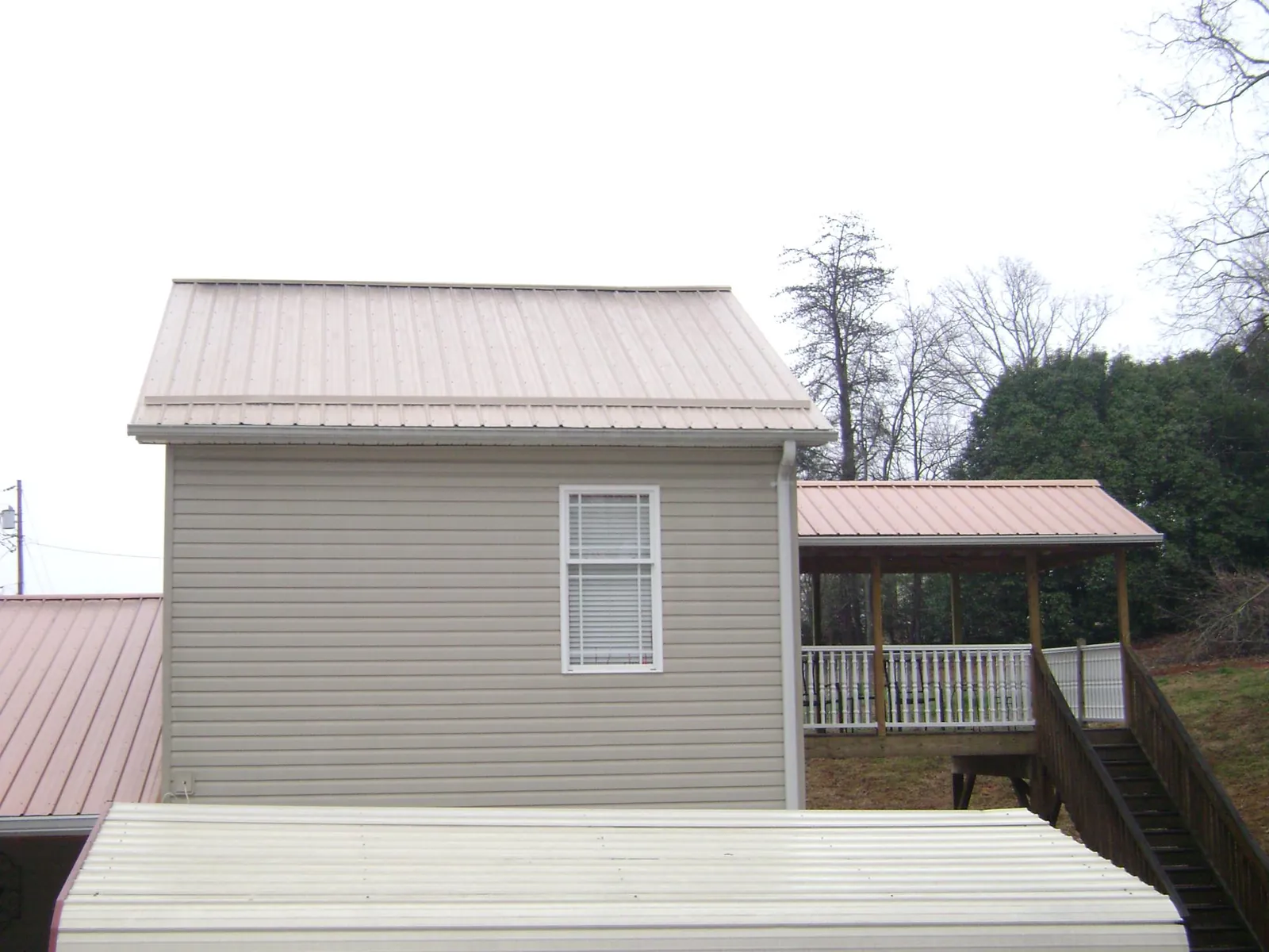 Tan metal roofs on a two story addition and attached porch, from a Roof Replacement job in Fort Morgan